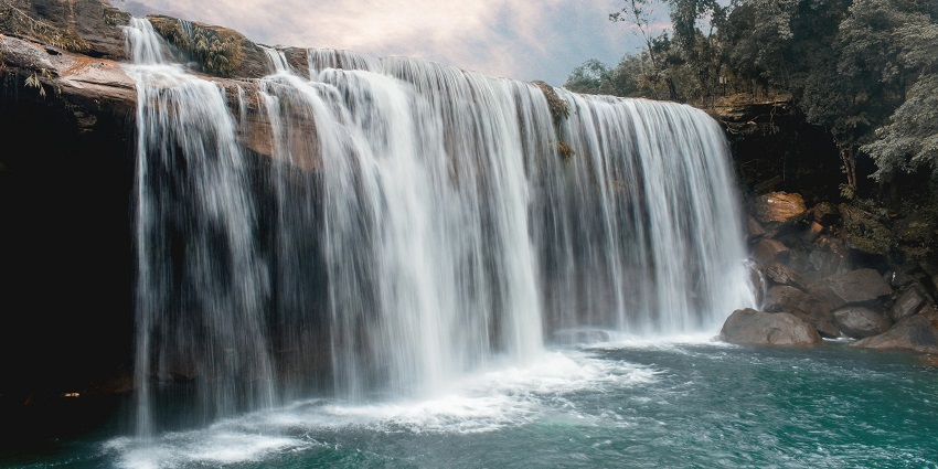 Scenic view of a waterfall during daytime, surrounded by lush greenery and rocks