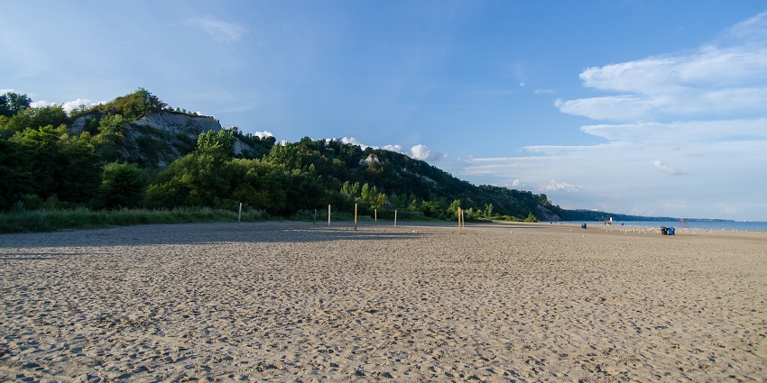 Bluffer’s Park Beach with sandy shoreline and the greenery is in contrast to the blue sky.