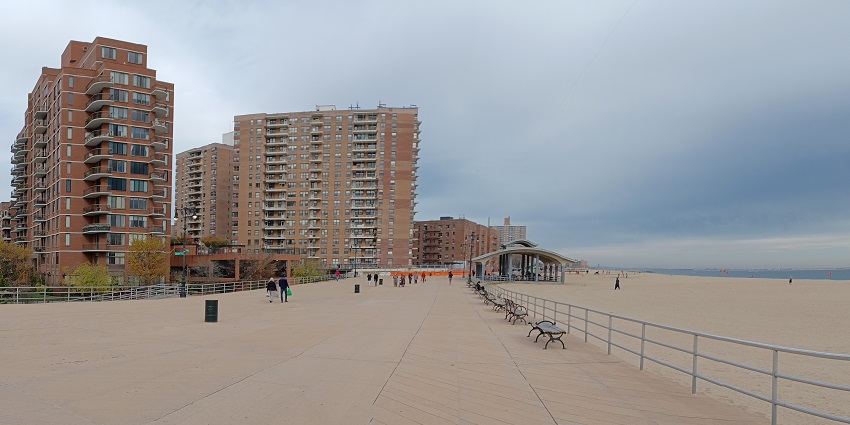 A row of brick and beige apartment buildings with balconies, situated on a sandy beach
