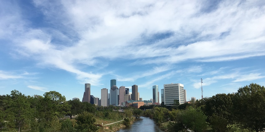 Buffalo Bayou Park with a small river, surrounded by greenery and tall skyscrapers