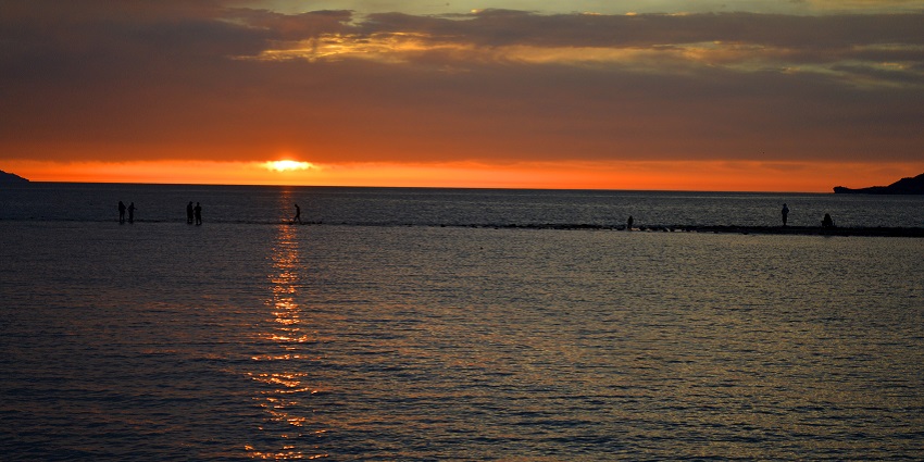 A few people are walking by the beach as well as enjoying a mesmerising sunset view
