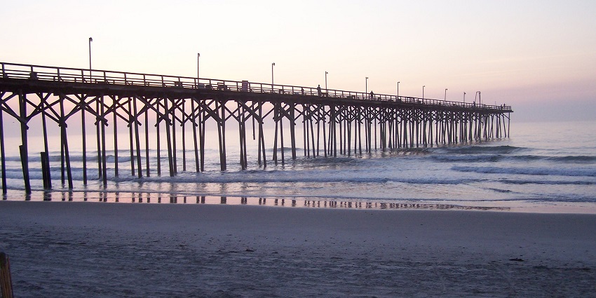 A vibrant view of Carolina Beach Pier stretching over the ocean under a partly cloudy sky.