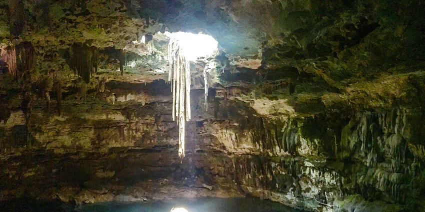 An inner view of a cenote that has clear water and on the upper side there is a hole