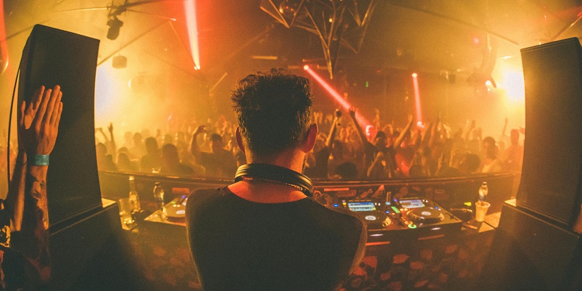 A crowd of people dancing inside a club with unique lights and a DJ playing music.