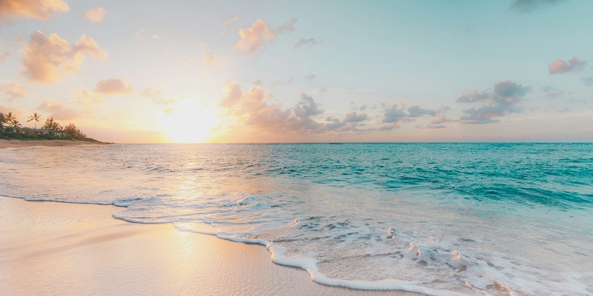 A scenic sunrise view can be seen on a pristine beach with a minimal lush green backdrop