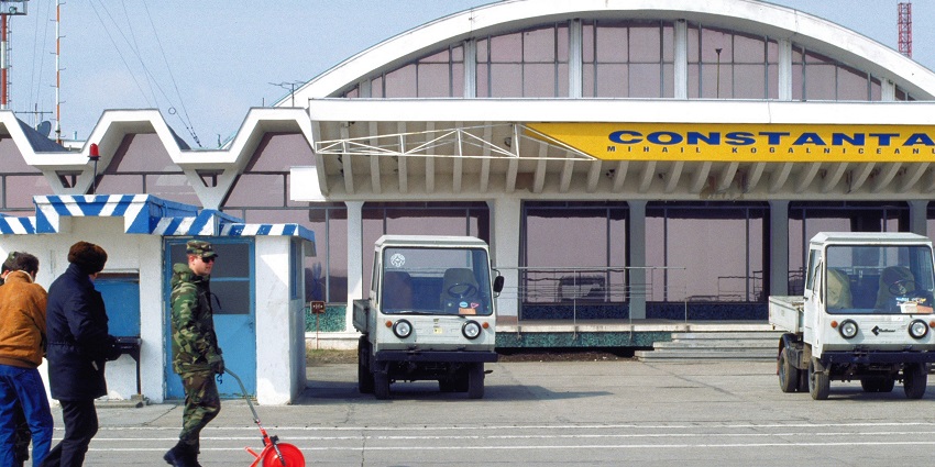 Outside of Constanța International Airport, small trucks are parked and people walking.