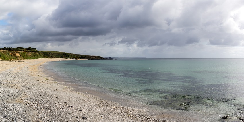A picture of a beach with white sand and blue waters along with trees and greenery