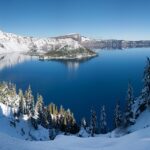 An image of the winter panorama of Crater Lake with snow-covered landscapes and icy blue waters.