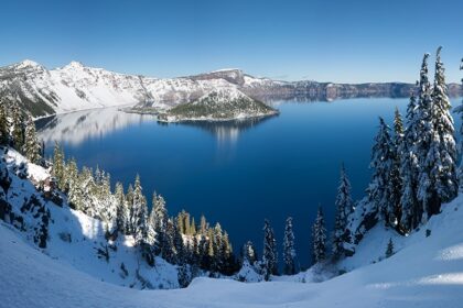 An image of the winter panorama of Crater Lake with snow-covered landscapes and icy blue waters.