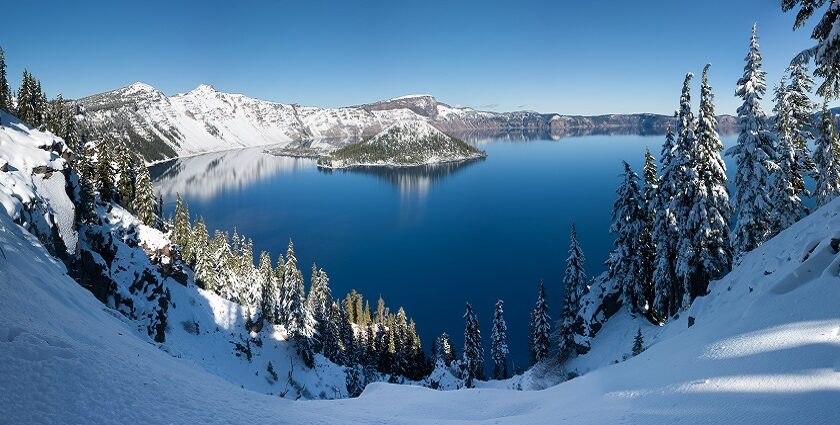 An image of the winter panorama of Crater Lake with snow-covered landscapes and icy blue waters.