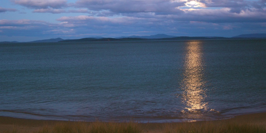 Moonrise over Cremorne Beach, Tasmania, with gentle waves under a twilight sky.