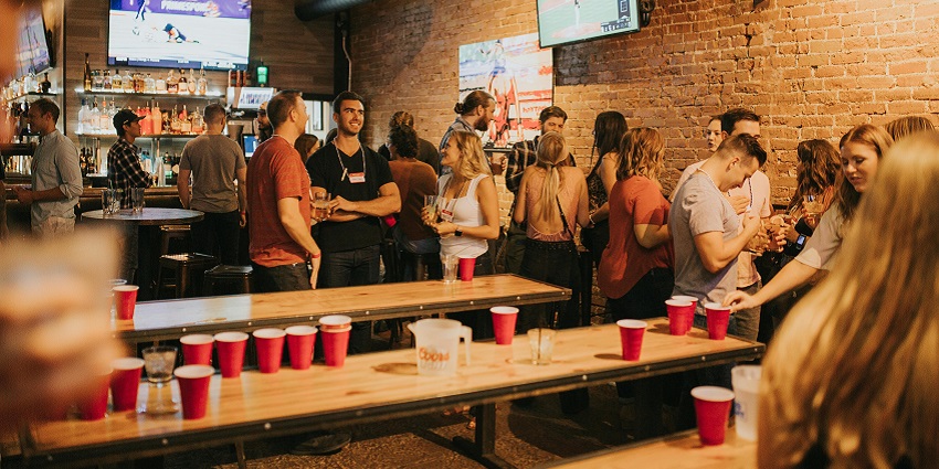 Inside the pub, people drinking and talking and multiple tables with plastic cups