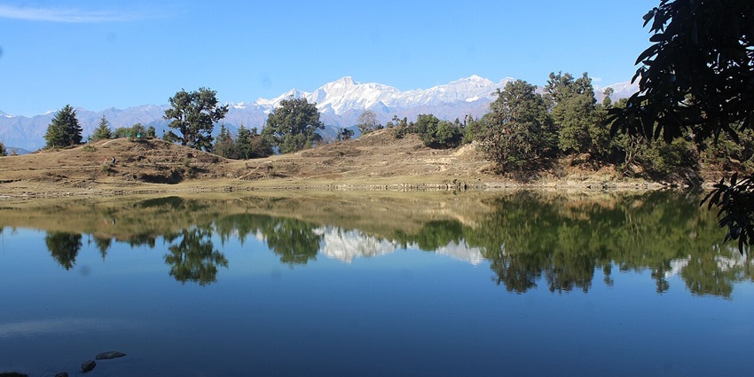 A frontal view of a serene lake with reflection of snow capped mountains in it