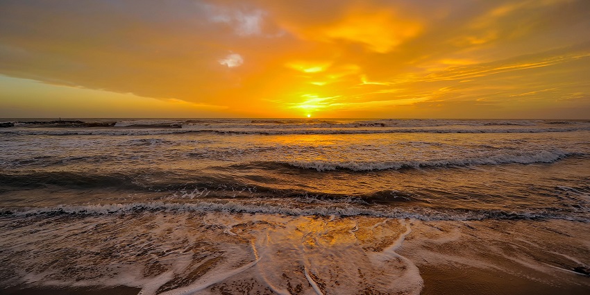 A peaceful beach scene at sunset with gentle waves, golden sand, and a colourful sky.