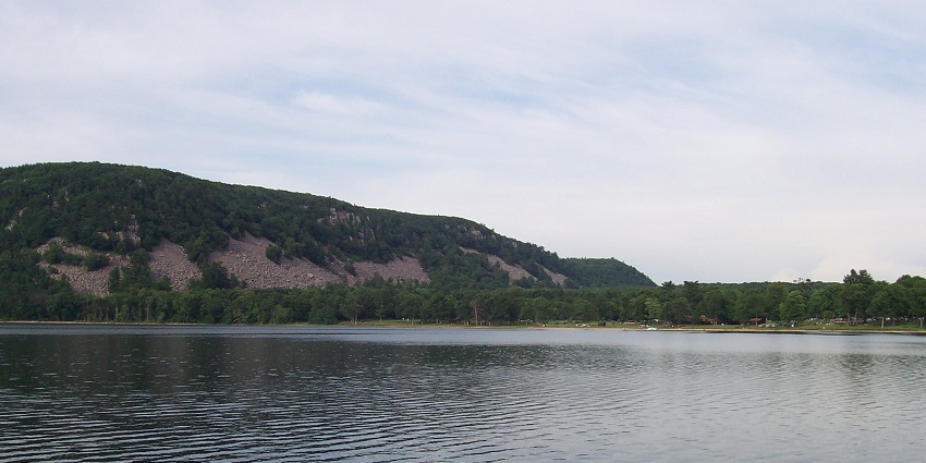 A wide view of Devil's Beach in showing sand, waves, and a bright sky and hills.