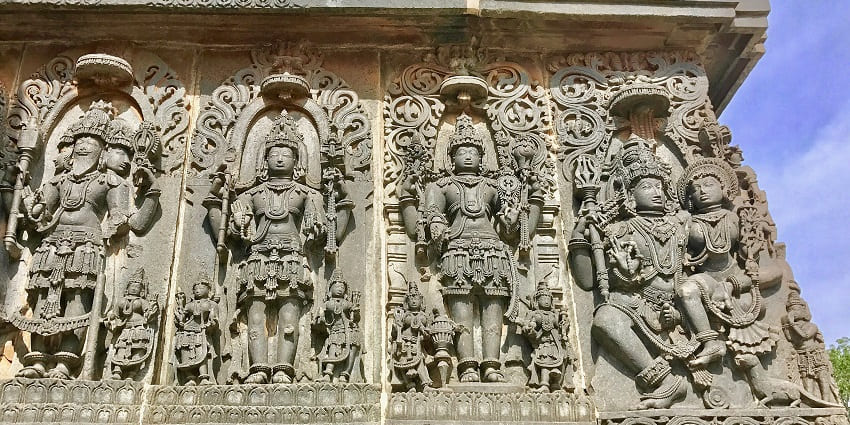 A picture of the exterior walls of a temple with intricate carvings of Hindu deities