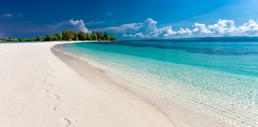 Calm waves washing ashore on a sandy beach with a clear blue sky in the background