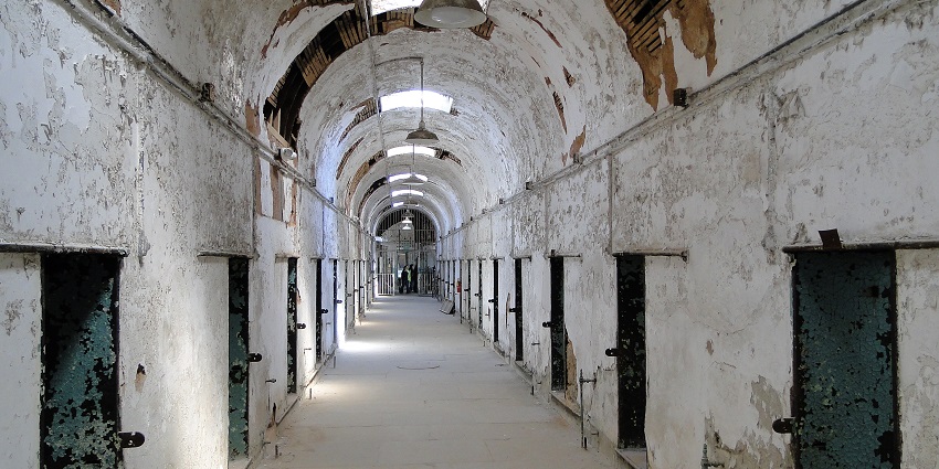 Halls of Eastern State Penitentiary with ruined walls, green doors and people exploring.