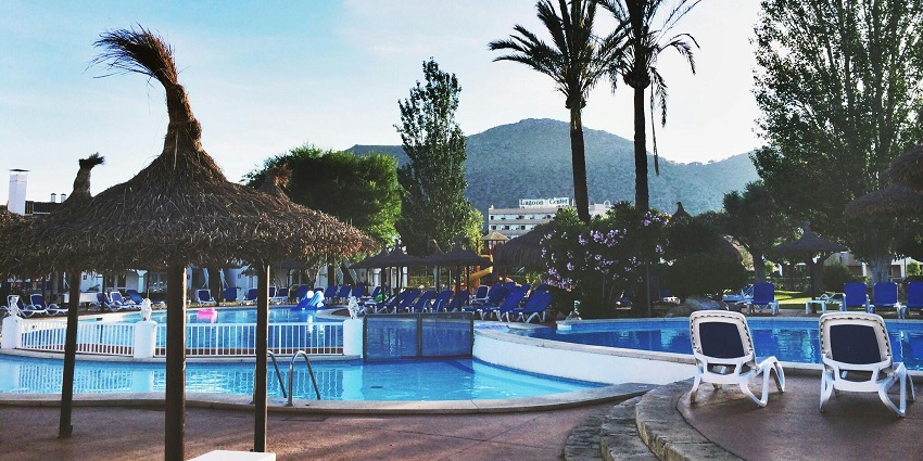 Scenic resort pool with a twisting water slide, palm trees, and loungers under sunny skies.