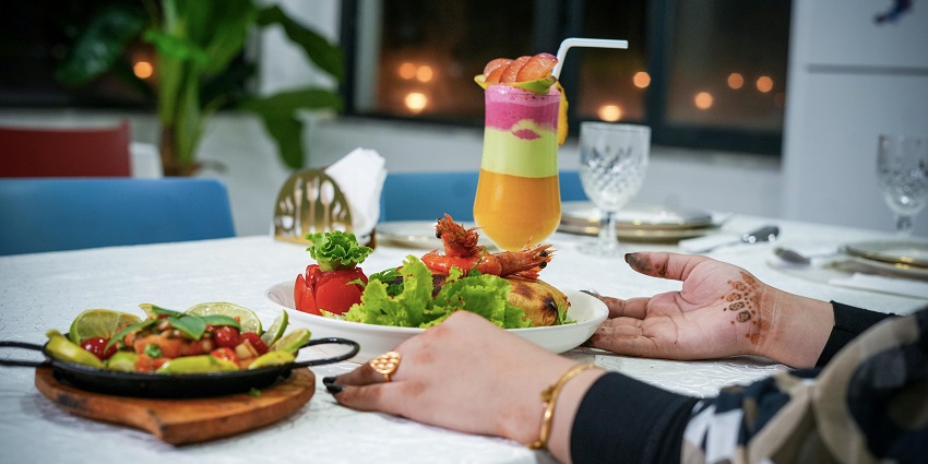 A colourful mocktail served with a well-garnished prawn at a table in a restaurant.
