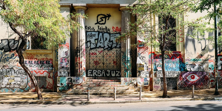 Street in Exarchia with an old building covered in graffiti and a couple of trees