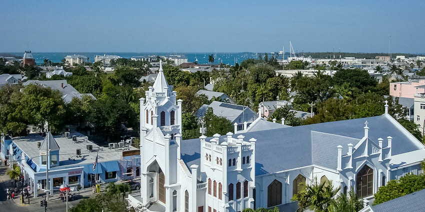 An aerial view of Key West shows a church with yachts sailing in the distant background