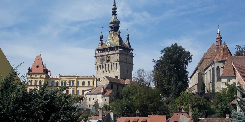 Old town of Sighişoara with old-style architecture, green trees and small flags on top
