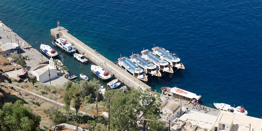 Tour boats parked at a small bay with people entering in the boat and small buildings