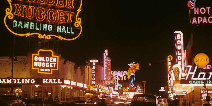 Fremont Street at night with illuminated shop names, gambling halls and cars parked