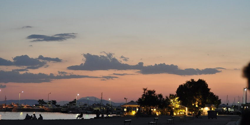 Glyfada in the evening with people sitting on chairs, street lights and distant mountains