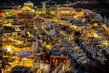 Greece at night with well-lit restaurants, clubs rooftop bars and a distant coastline