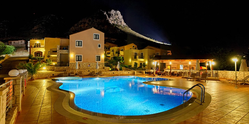 Empty luxury villa complex with a pool, poolside chairs and shiny Creta mountains