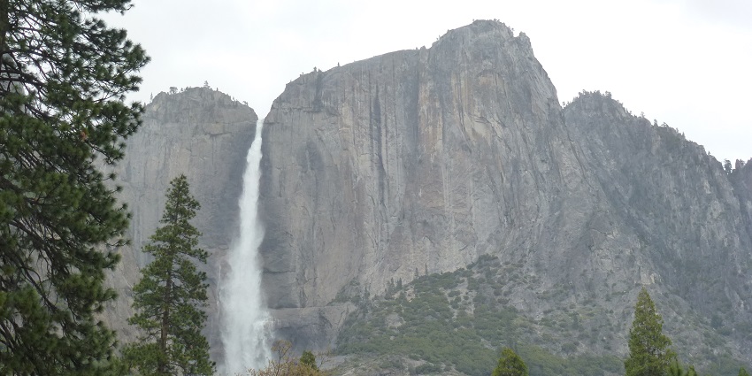 An image of Horsetail Falls, with water cascading down the rocky cliffs, framed by trees and mountains