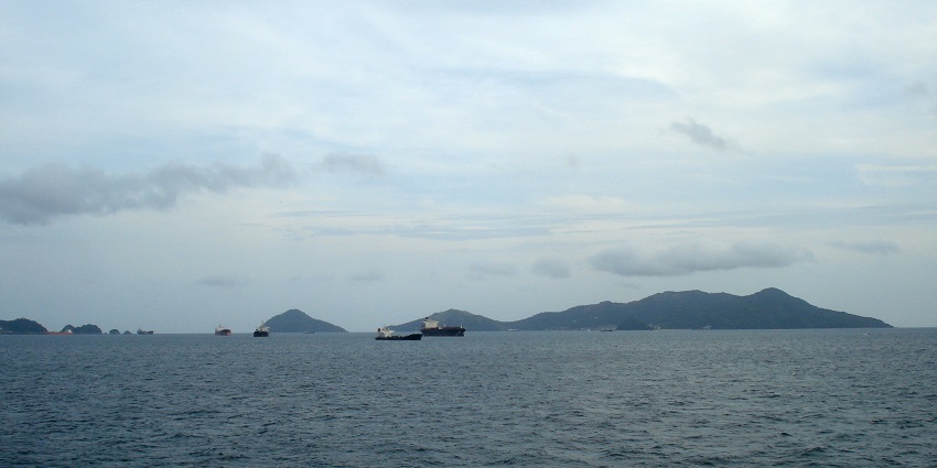 An image of ships docked at a harbour with coastline and cloudy sky in the background.