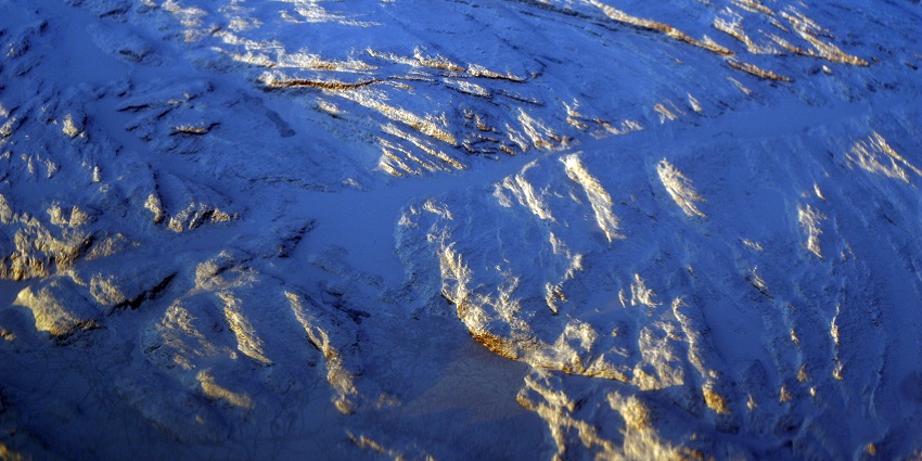 An aerial view of Nunavut's snowy landscape, featuring rugged terrain and scattered shadows.