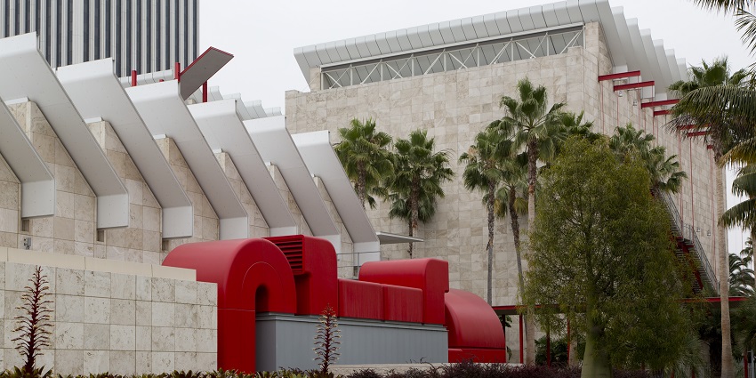 Wide view of LACMA's main buildings with palm trees and visitors walking nearby