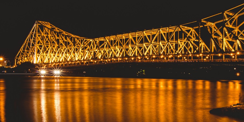 A picture of the Howrah Bridge at night with vibrant lights reflecting on the water below.