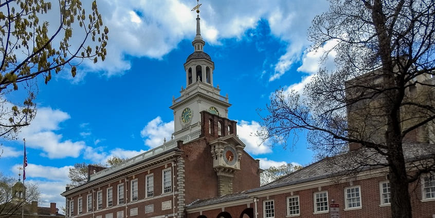 Independence Hall from the side with its building and complex against a cloudy blue sky.