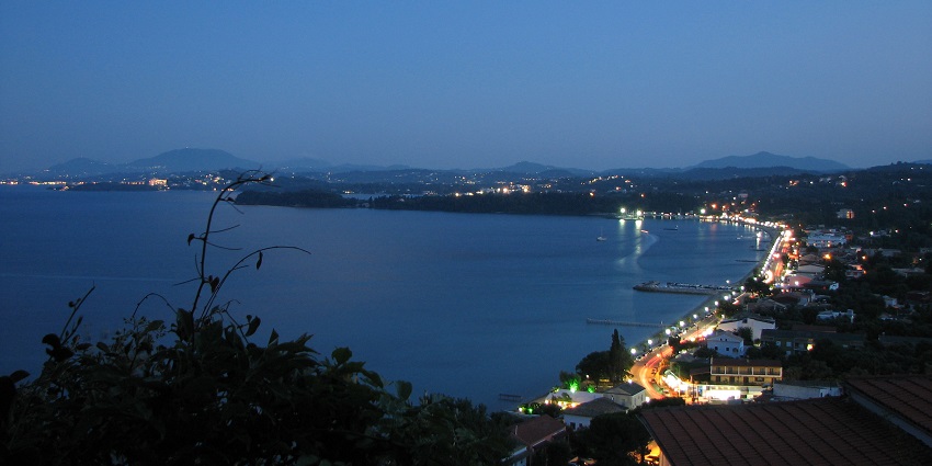 Ipsos Beach coastline from above with lit roads and small buildings spread on the hills