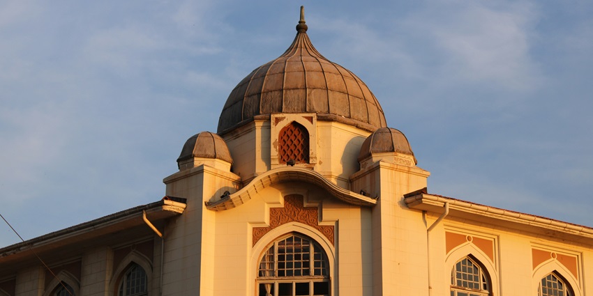 An Islamic building with a prominent dome and arched windows under a partly cloudy sky.