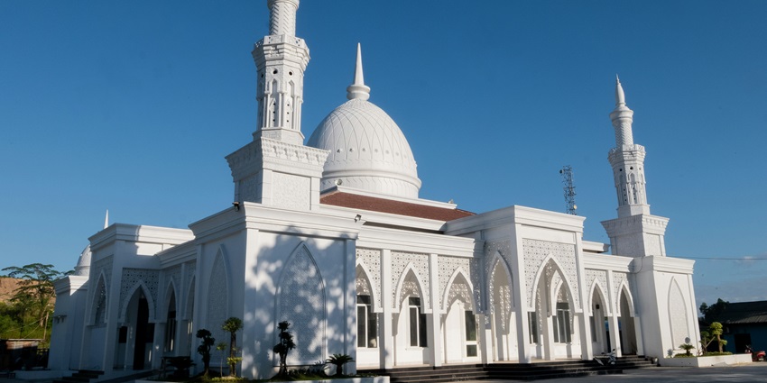 An image of a large, white mosque with domes and minarets stands under a clear blue sky.