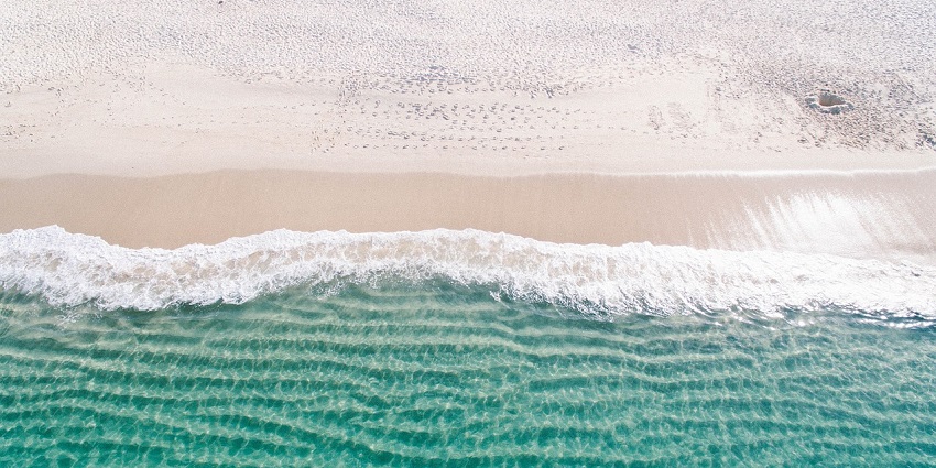 A calm beach with golden sand, gentle waves, and clear blue water under a bright sky.