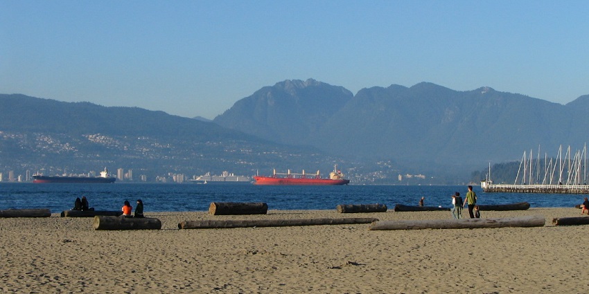 A long stretch of Jericho Beach with logs placed is facing a beautiful mountain view.