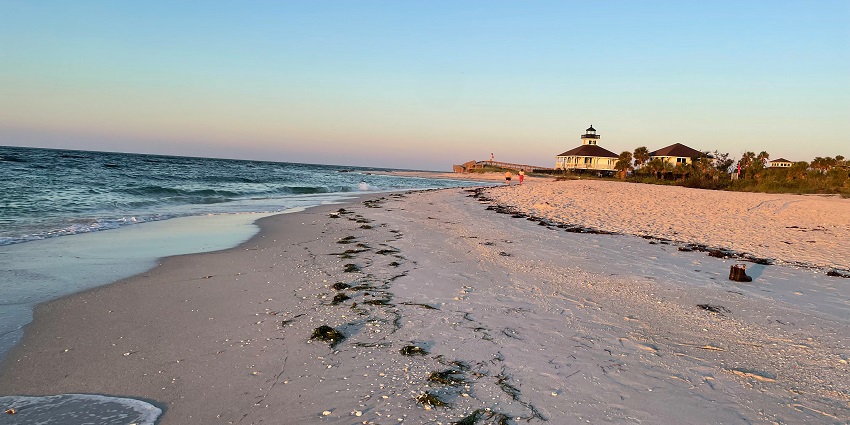 White sand has turned pink on a beach with a lighthouse during the time of sunset