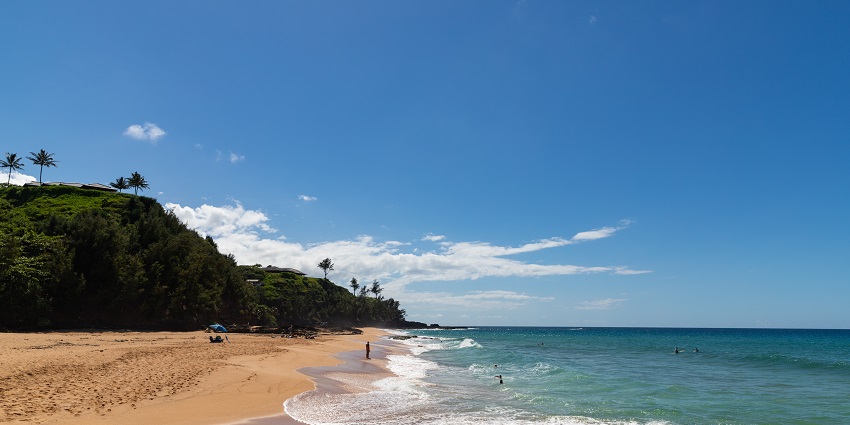 Leisurely waves are crashing on golden sands, bordered by jungle-covered cliffs