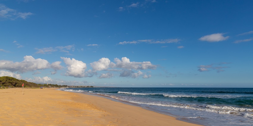 View of Kekaha Beach in Kauai, Hawaii, with clear blue waters and gentle waves.