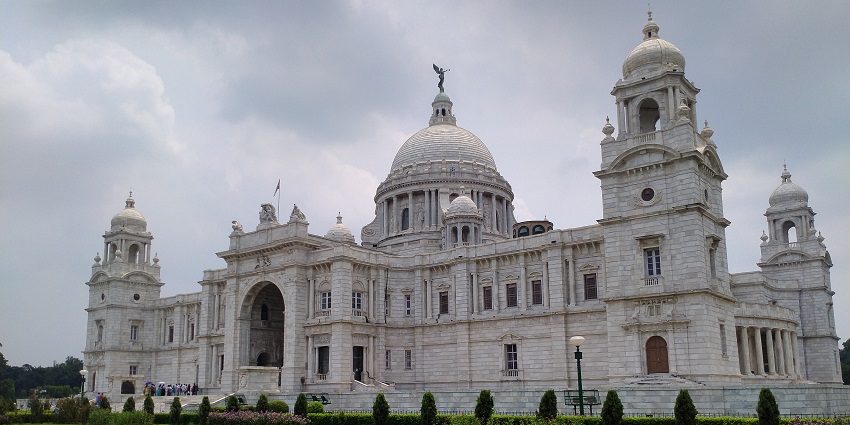 An image of Victoria Palace in Kolkata with a dome and several towers set on a lush green lawn.