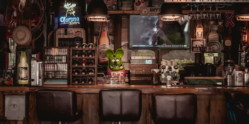 Bar countertop with multiple chairs, alcohol bottles and a television in the background