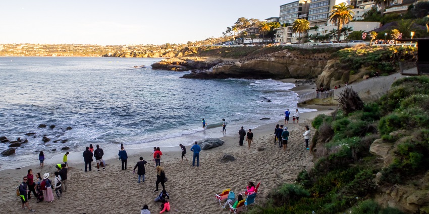 A view of the LA Jalla Cover beach with people relaxing in the sand and buildings nearby