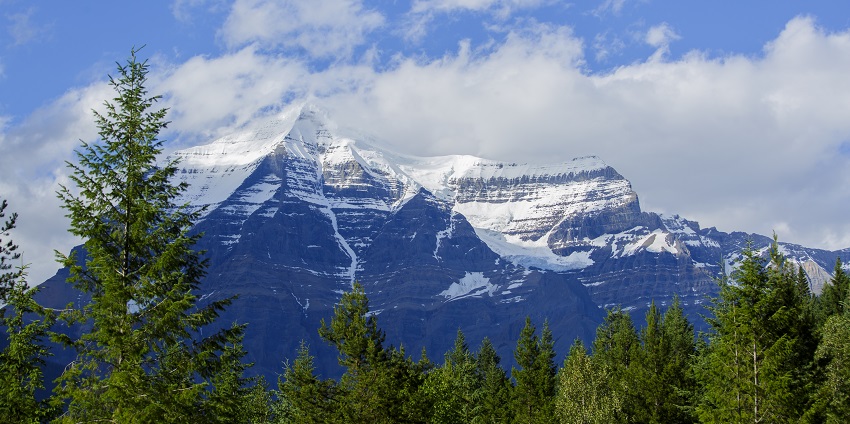 A majestic mountain range in Jasper National Park, partially hidden by clouds and trees